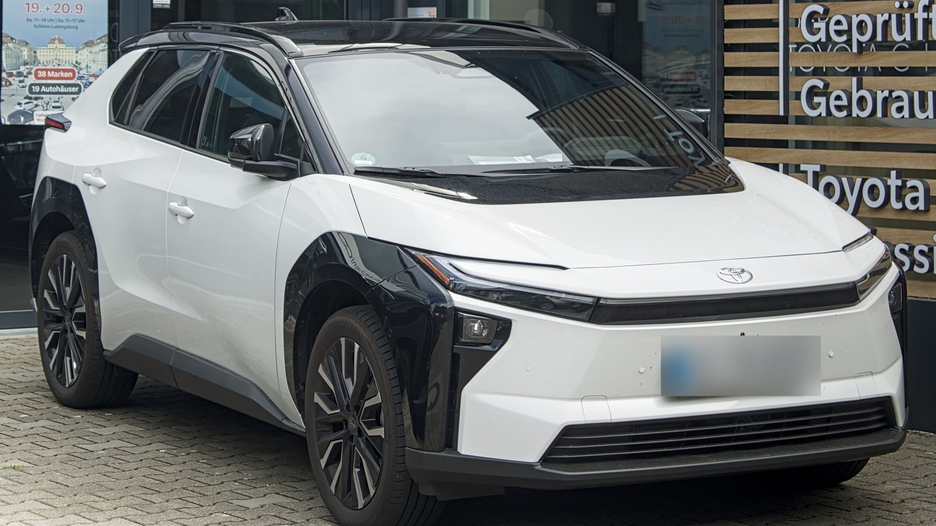 Λευκό Toyota bZ4X μοντέλου 2026 σταθμευμένο μπροστά σε έκθεση Toyota, μπροστινή τρία τέταρτα